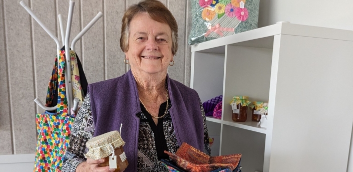 Keen crafter, Cheryl Johnson holding a few of her handmade crafts, including jam covers and small handkerchiefs in Samford Grove's library.