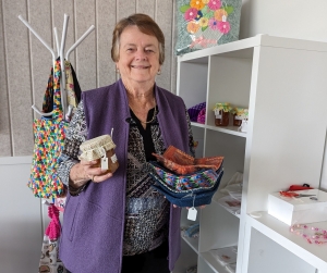 Keen crafter, Cheryl Johnson holding a few of her handmade crafts, including jam covers and small handkerchiefs in Samford Grove's library.