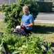 Resident Margaret Crombie wearing gardening gloves and sitting in a green garden and veggie patch.