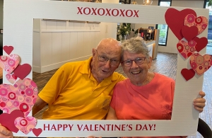 Samford Grove residents Don and Daphne holding a large Valentine's Day photo frame. Woman wears a pink t-shirt and man in yellow shirt.